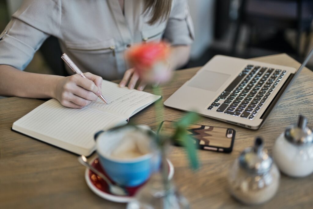 Woman writing and creating new content on a desk with office items.