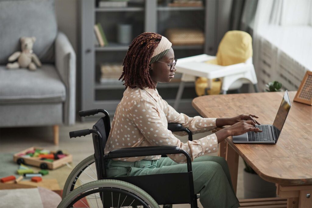 High angle portrait of young African-American woman using wheelchair while working from home with childrens toys in background, copy space