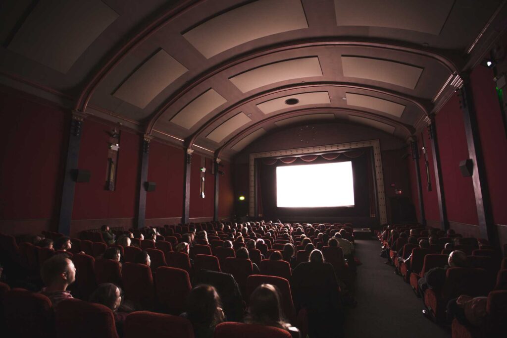 A cinema theater displaying a movie with seated people watching.